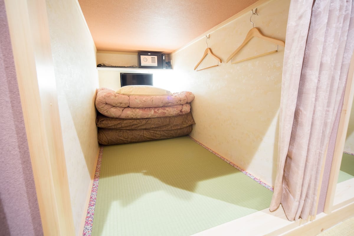 A small, compact room with a futon bed, a microwave, and a wooden hanger.