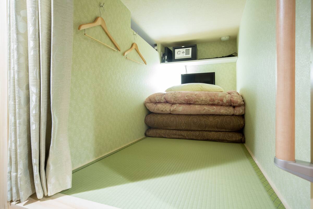 A small, narrow room with a bed, a radio, and a wooden hanger on the wall.