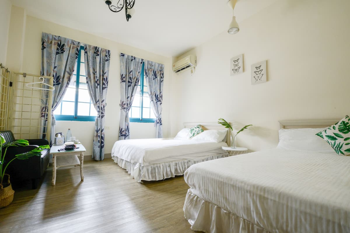 A hotel room with two beds, a small table with a plant, a hanging chair, and a window with curtains.