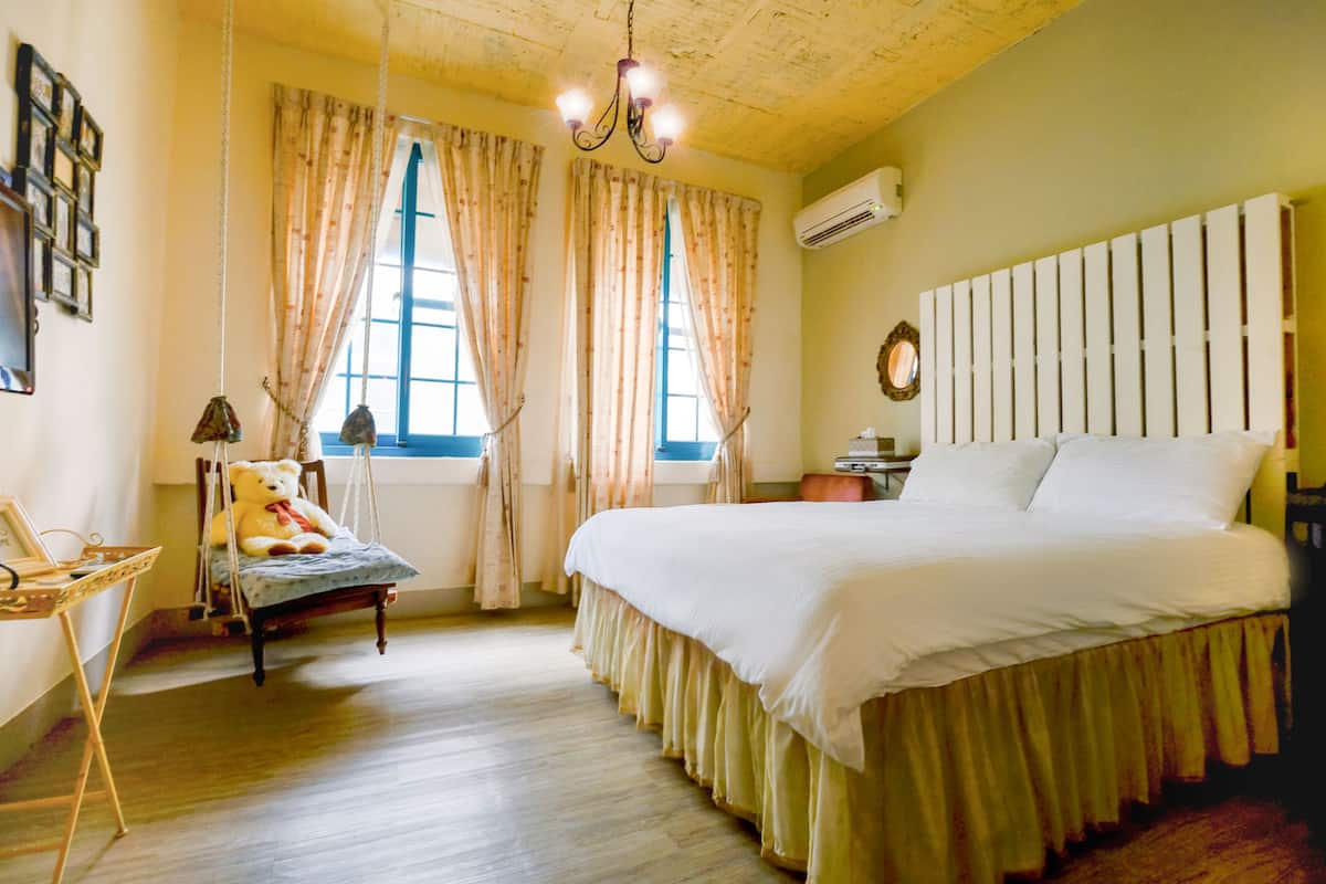 A bedroom with a bed, a chair, a window, and a chandelier.