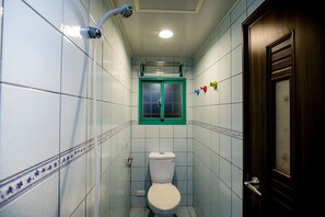 Un baño pequeño con azulejos blancos, inodoro, ducha y puerta con ventana.