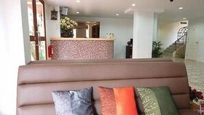 A living area with a sofa and cushions, a reception desk, and a staircase. - Roof View Place (Bangkok)
