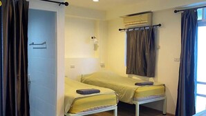 A room with two beds, a ceiling fan, an air conditioning unit, and a window with curtains. - Roof View Place (Bangkok)
