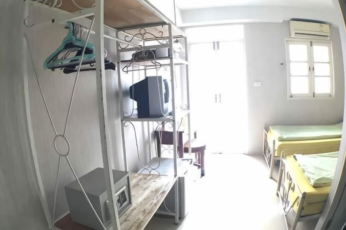 A dormitory room with bunk beds, a desk, a chair, a TV, and a wardrobe.