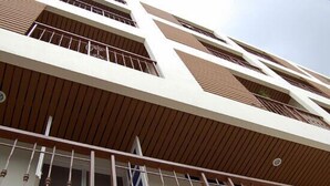 A multi-story building with a modern architectural design, featuring a combination of wooden paneling and white walls. - Roof View Place (Bangkok)