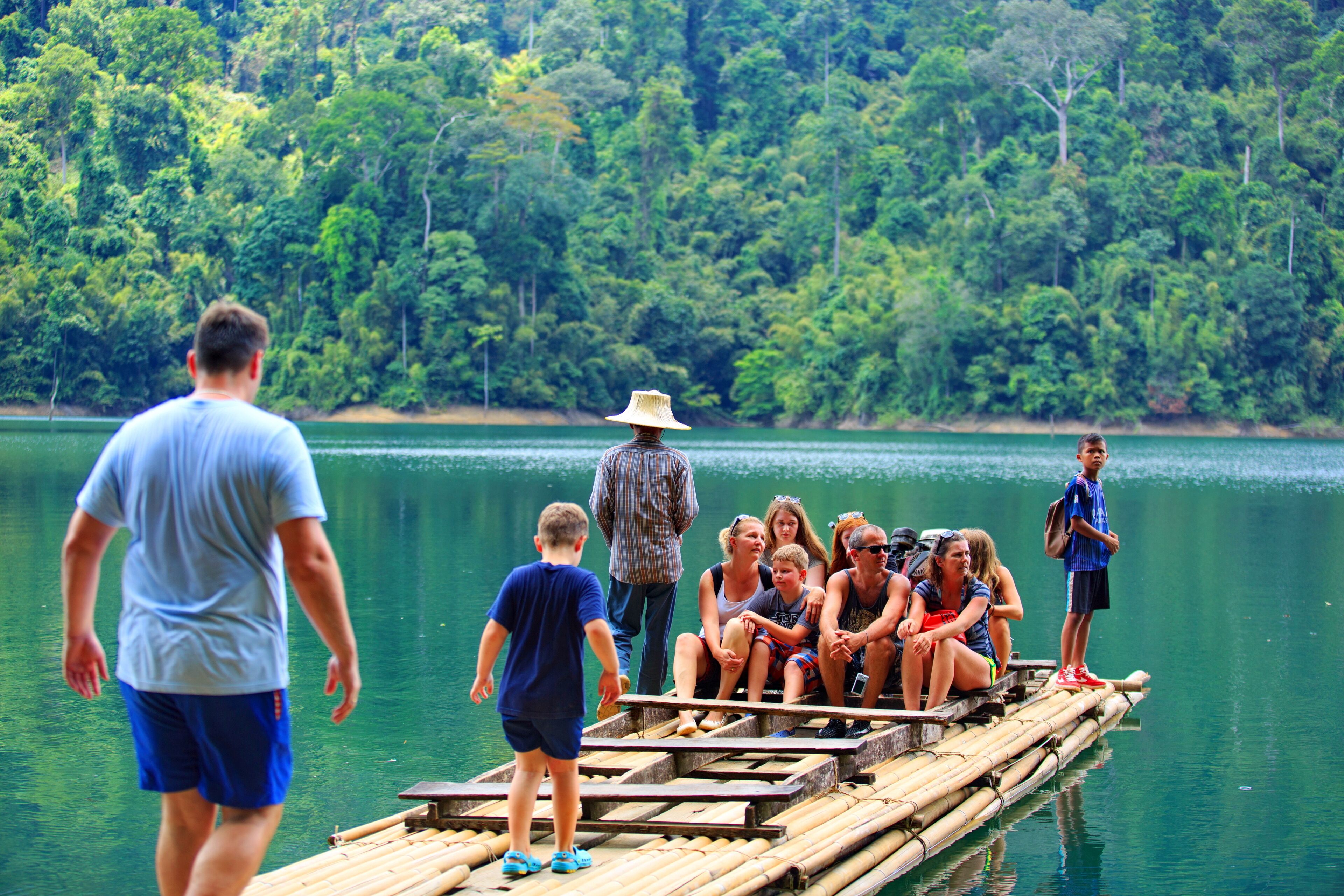 A group of people on a bamboo raft in a lake surrounded by dense forest.