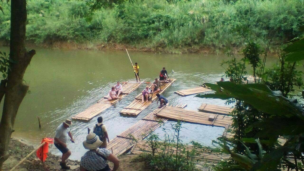 Eine Gruppe von Menschen auf Bambusflößen in einem von Grünpflanzen umgebenen Fluss.
