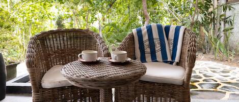 A wicker chair with a cushion and a small round table with a cup and saucer.