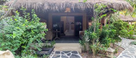 A thatched-roof structure with a stone pathway leading to it, surrounded by lush greenery.