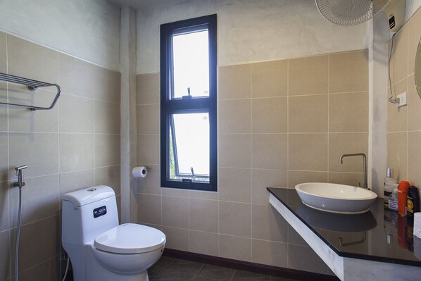 A bathroom with a toilet, a sink, a window, and a shower.
