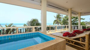 Un espace piscine avec vue sur l’océan, des chaises longues dotées de coussins rouges et une rambarde blanche.