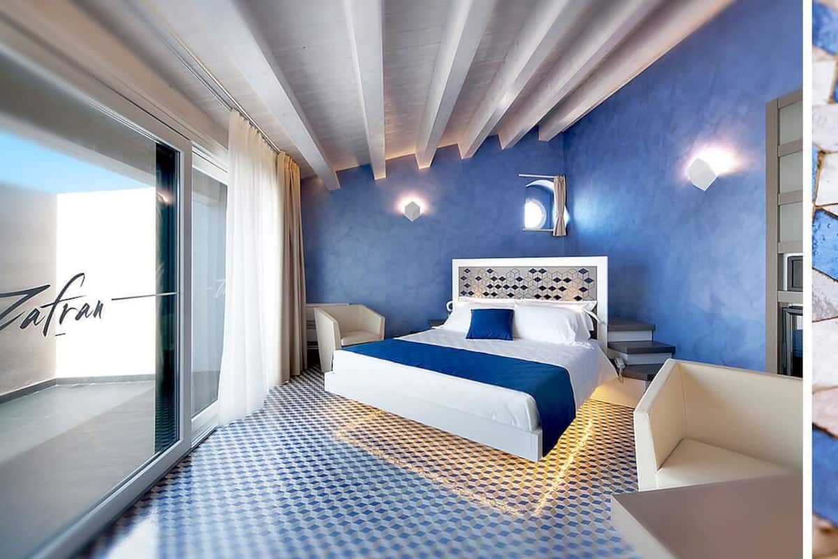 A modern hotel room with a large bed, a desk, and a view of the sea.