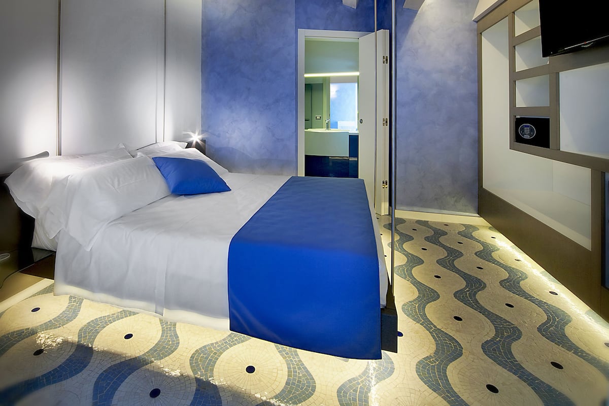 A modern hotel room with a bed, a TV, and a bathroom visible through an open door.