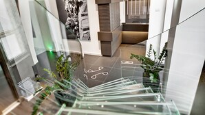 A modern interior with a glass staircase, decorative wall art, and potted plants. - Zafran Boutique Hotel (Scicli)