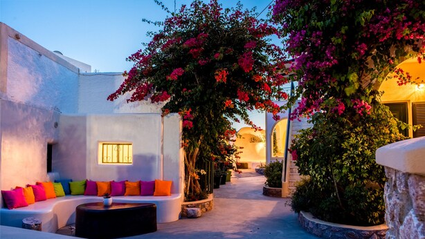 A courtyard with a white sofa set, a round table, and a large flowering tree. - Paul's Studio (Santorini)