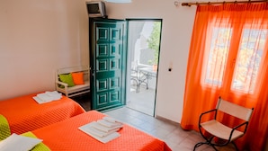 A room with two beds, a chair, a TV, and a door leading to an outdoor area. - Paul's Studio (Santorini)