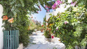 A narrow alleyway with lush greenery and flowering plants on either side. - Paul's Studio (Santorini)