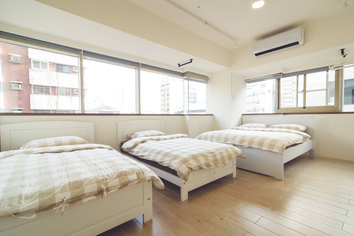 A room with three beds, large windows, and an air conditioning unit.