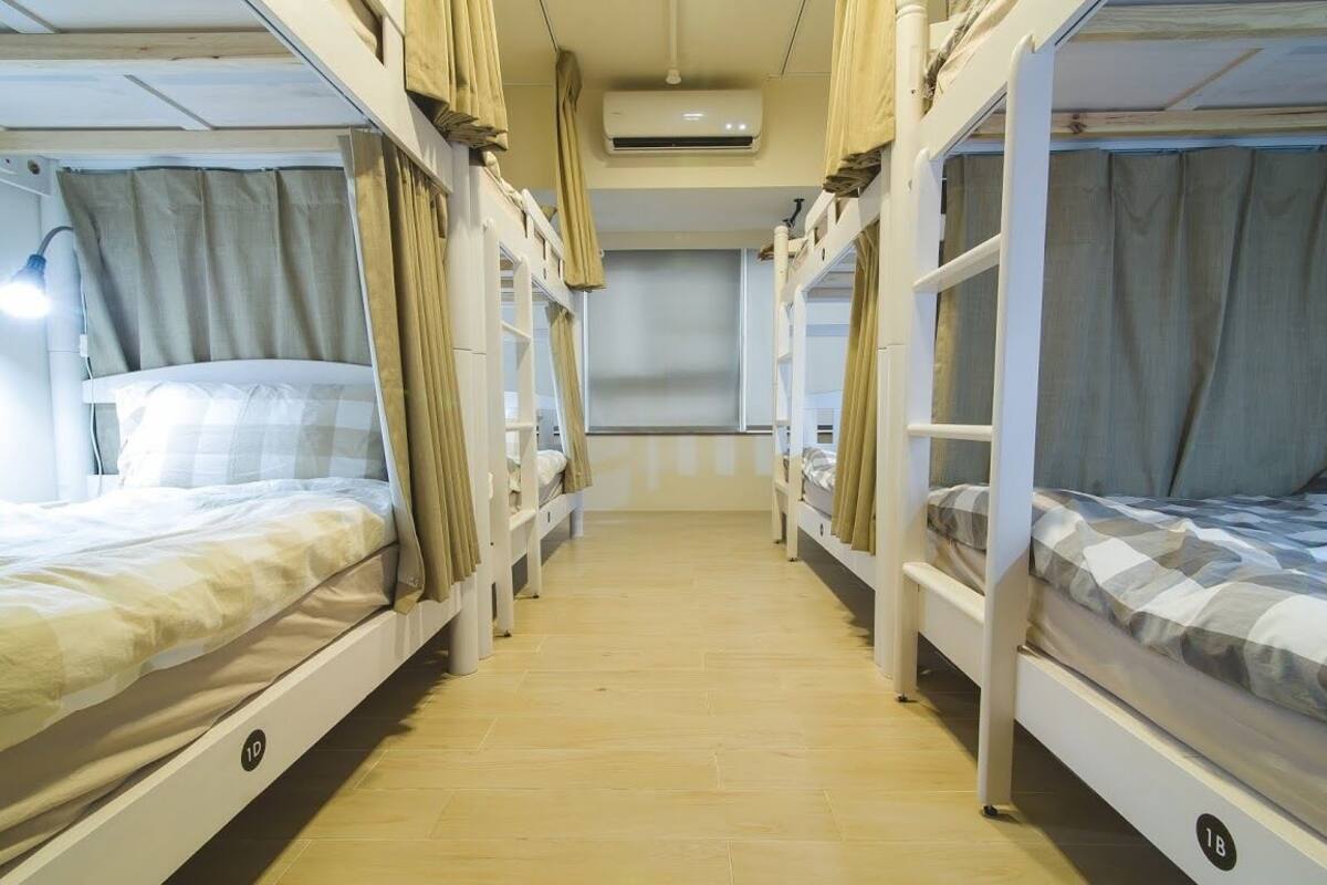 A corridor with bunk beds, each with a curtain, and an air conditioning unit above.