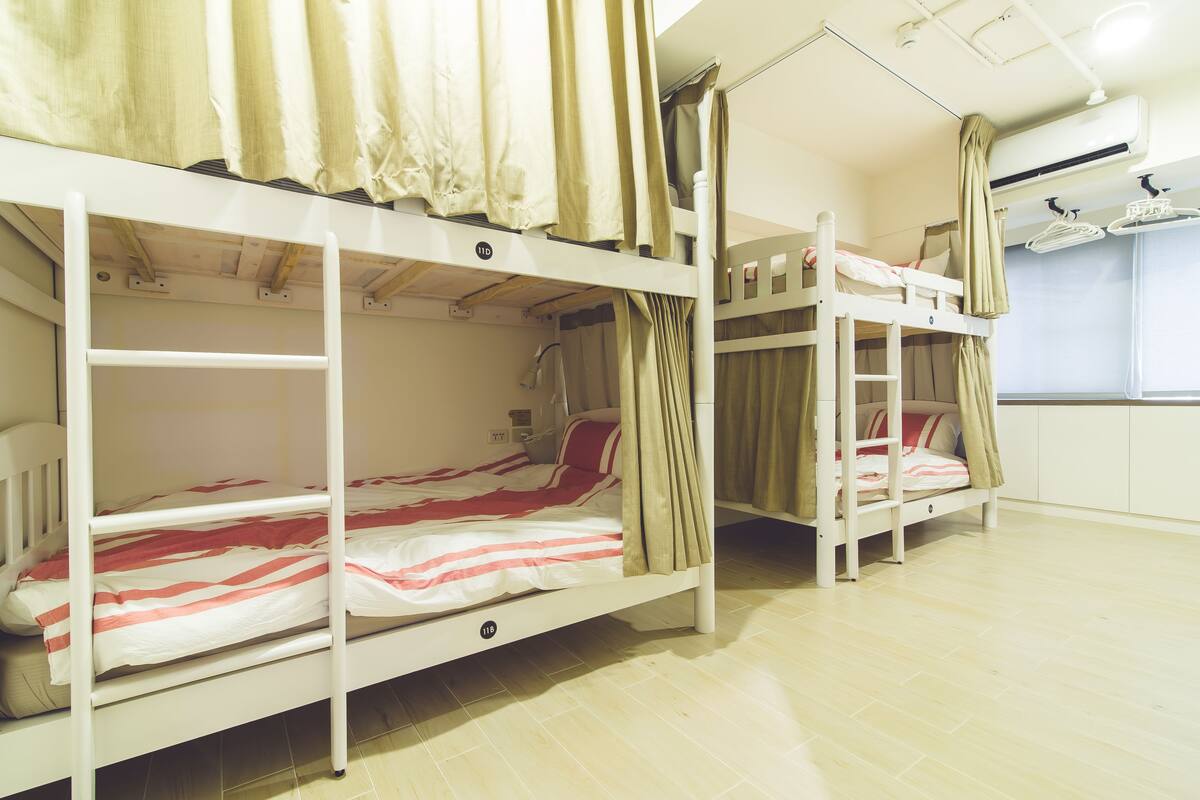 A room with bunk beds, a window, and a white wall with a curtain.