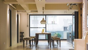 A modern dining area with a central table and chairs, large windows, and a view of the city. - Ahiruyah Guest House in Kaohsiung - Hostel (Kaohsiung)