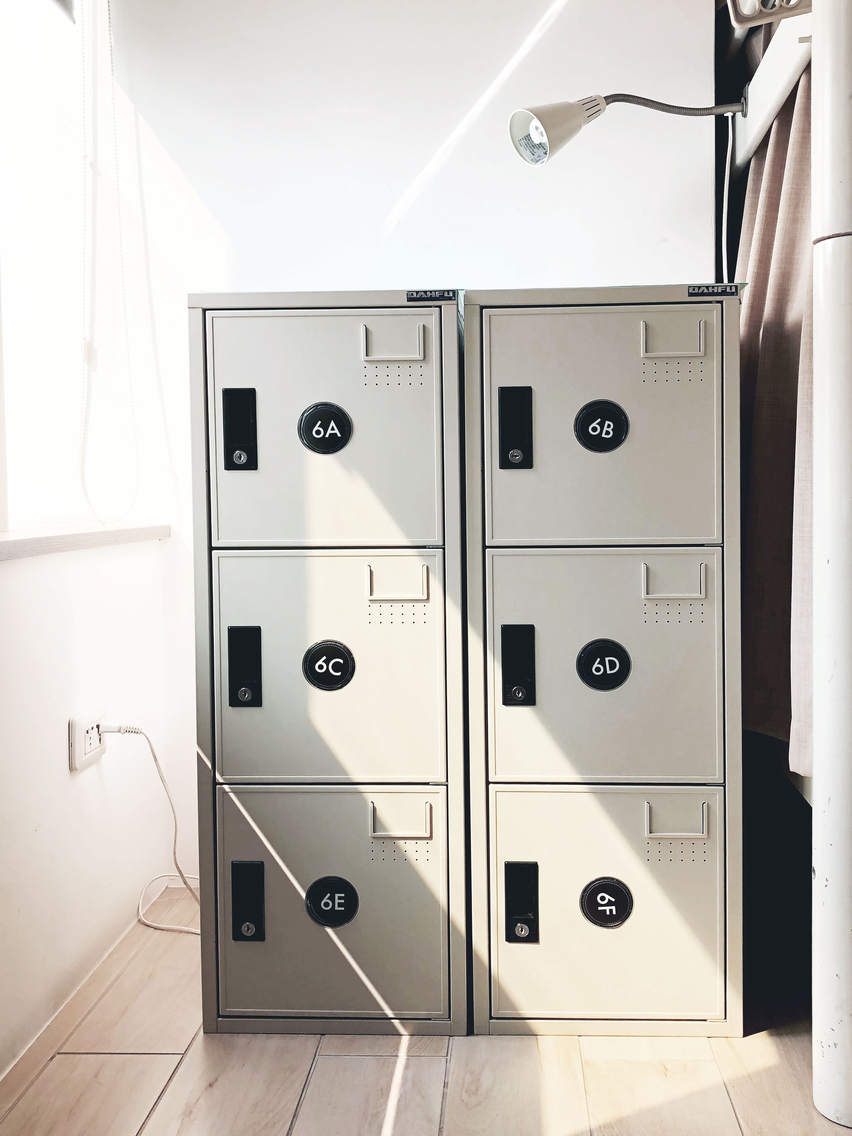 Two metal filing cabinets with labels 6A to 6F, a lamp, and a power outlet on a wooden floor.