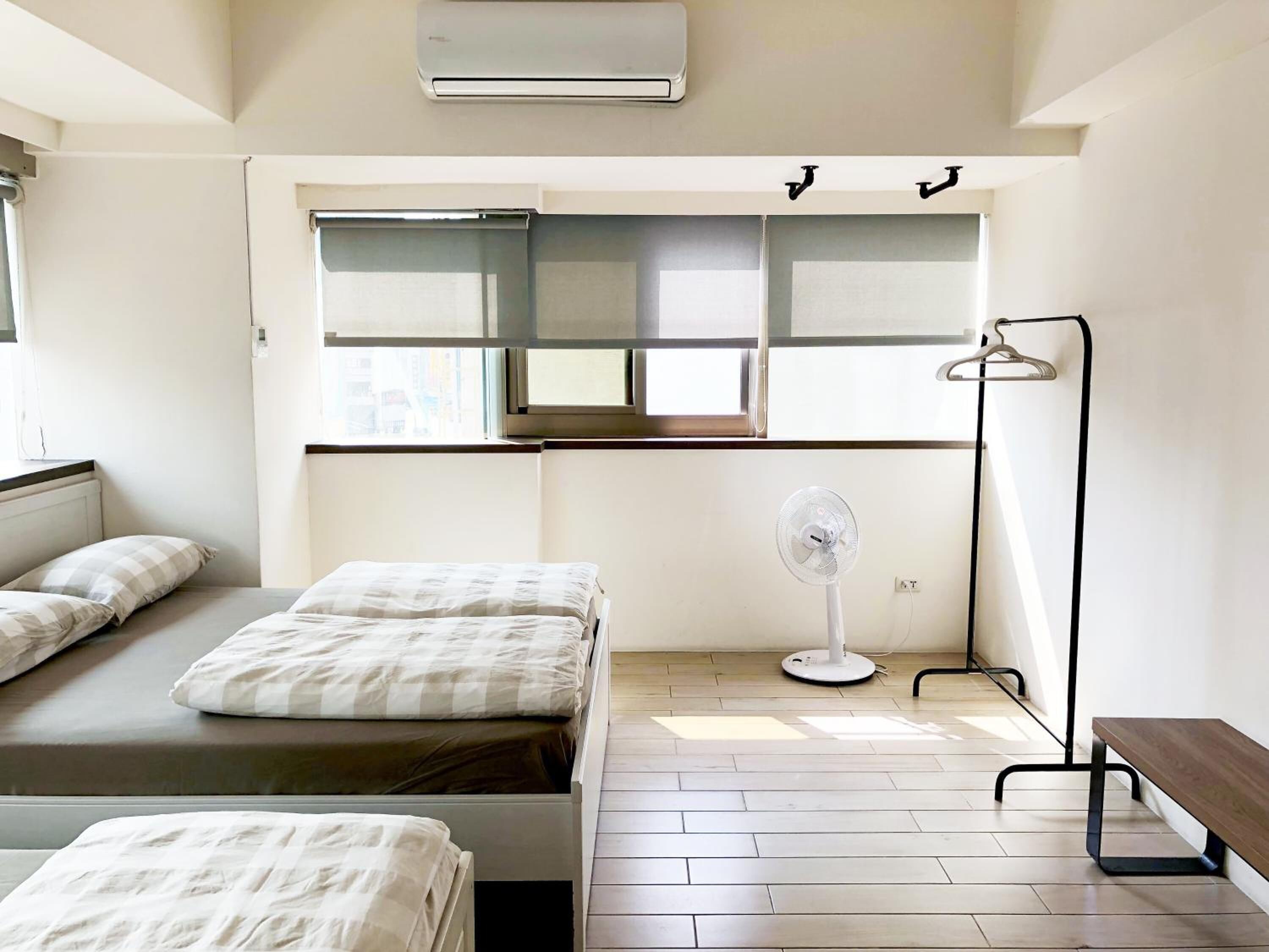 A hotel room with a bed, a bedside table, a standing fan, and a window.