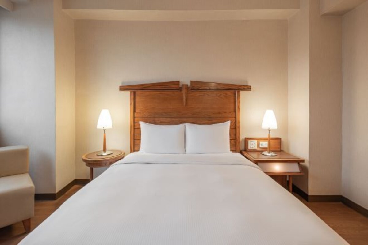 Habitación de hotel con una cama grande, dos mesitas de noche con lámparas y una silla.