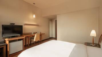 Een hotelkamer met een bed, een bureau met een televisie, een stoel, een lamp en een kleine koelkast.