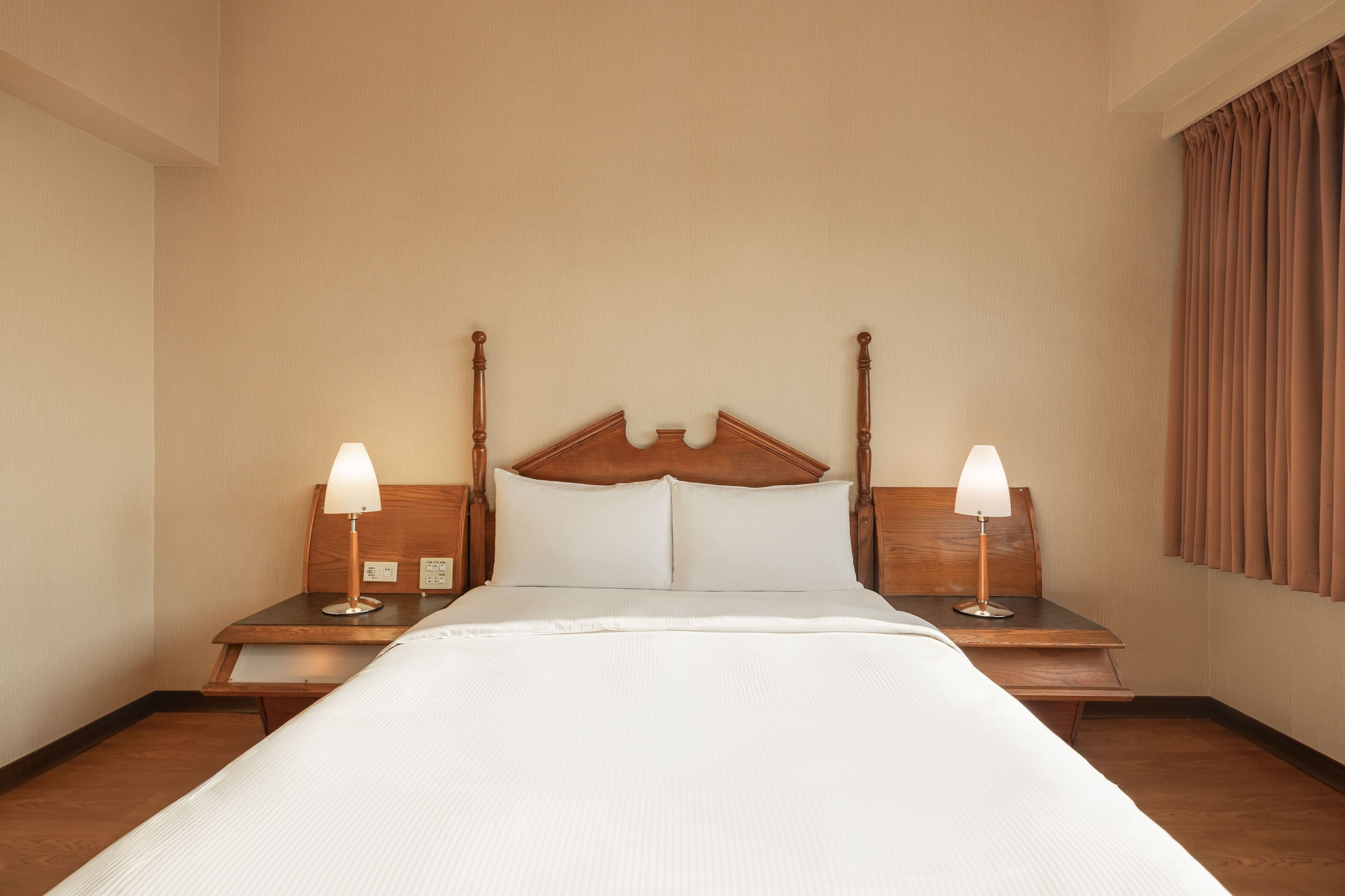 A hotel room with a large bed, two bedside tables with lamps, and a wooden headboard.