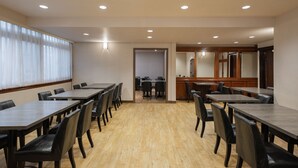 Una sala de conferències amb diverses taules i cadires, terres de fusta i llums incrustades al sostre.