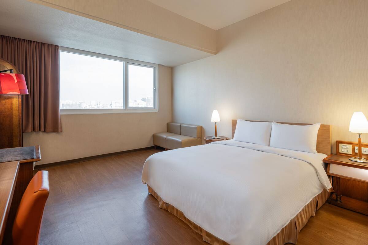 Habitación de hotel con una cama grande, un escritorio, una silla, un sofá y una ventana con cortinas.