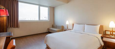 Ein Hotelzimmer mit einem großen Bett, einem Schreibtisch, einem Sessel, einer Couch und einem Fenster mit Vorhängen.