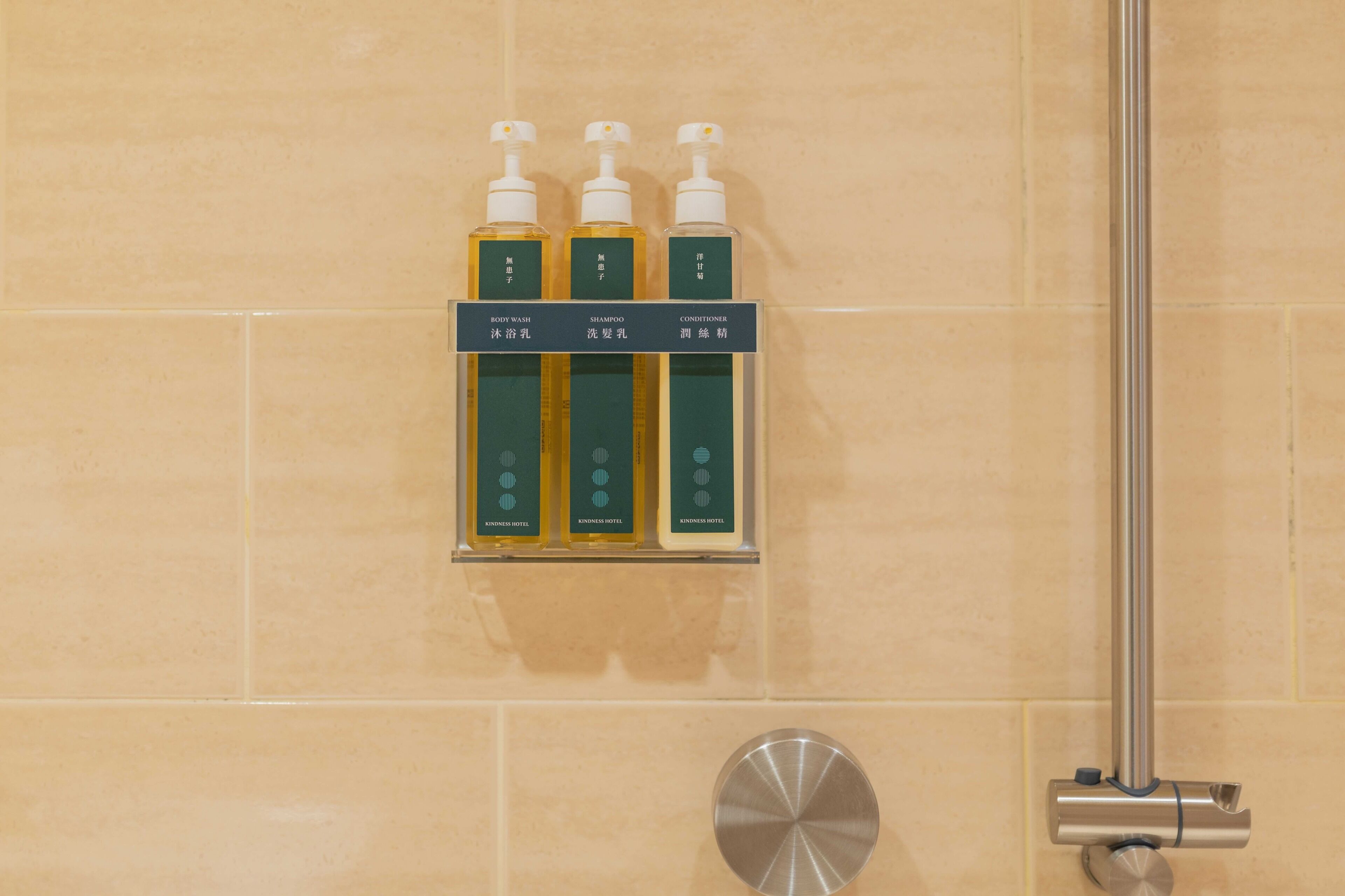 Un baño con un estante que contiene tres botellas de artículos de aseo, etiquetadas como 'BODY WASH', 'SHAMPOO' y 'CONDITIONER', cada una con dosificador tipo bomba.