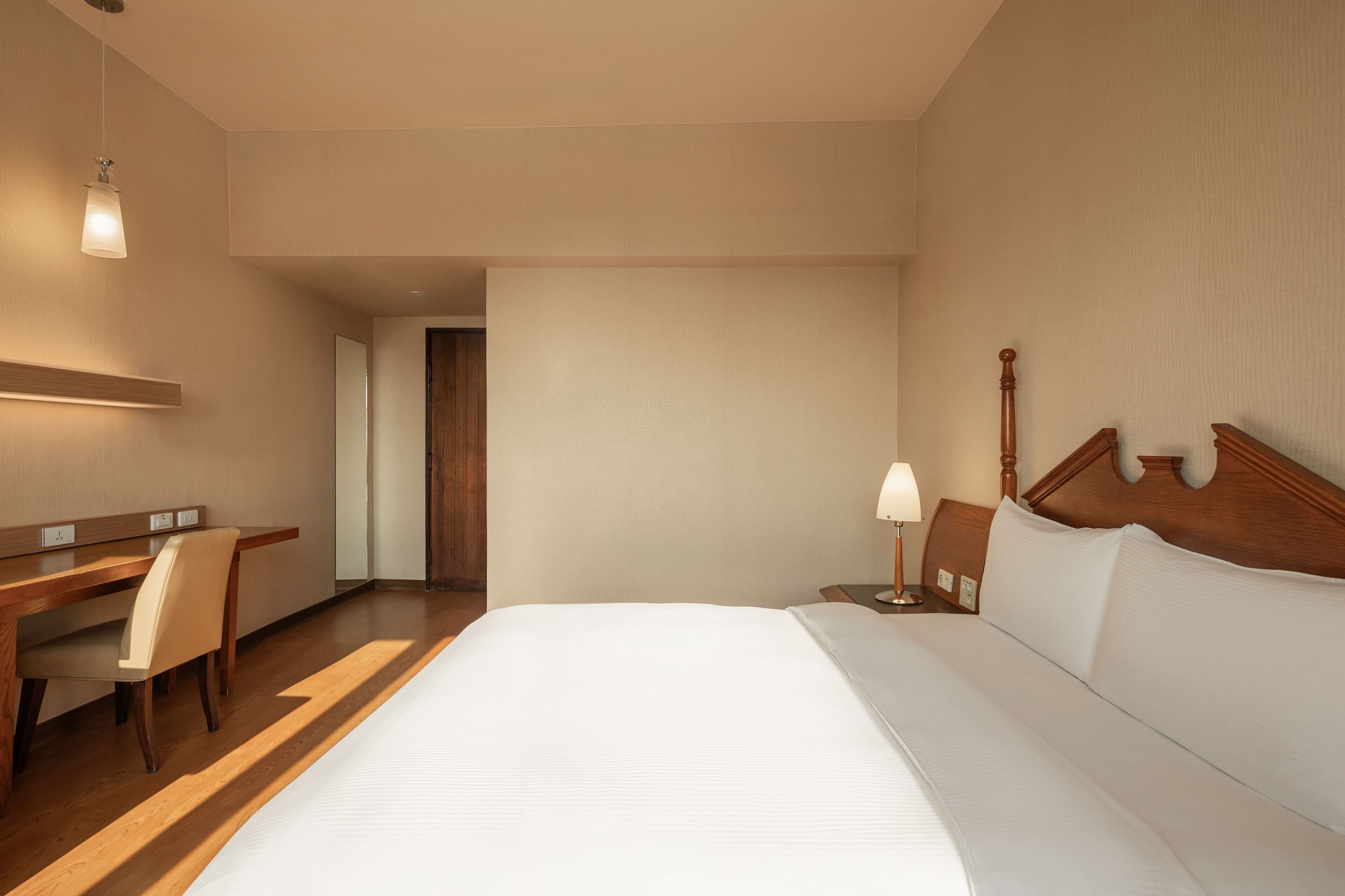 Een hotelkamer met een groot bed, een bureau, een stoel en een nachtkastje met een lamp.