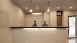 Taulell de recepció amb dos empleats, interior modern amb il·luminació empotrada i vista a l'exterior per una porta de vidre.