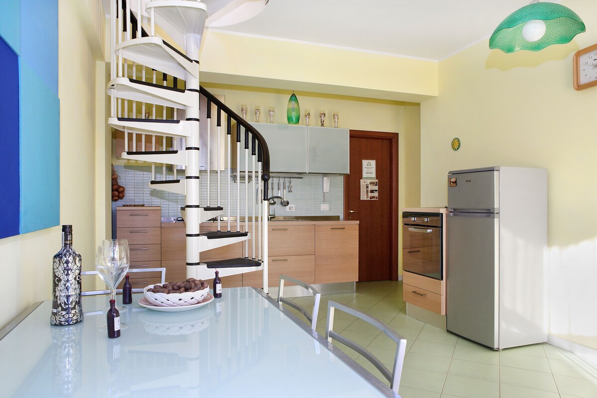 A modern kitchen with a spiral staircase, a dining table with chairs, and a refrigerator.