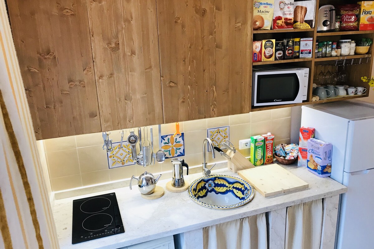 A kitchen with a wooden cabinet, a microwave, a sink with a decorative backsplash, and various food items on the counter.