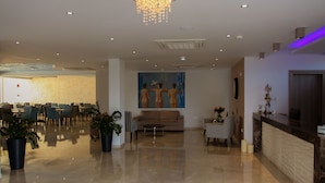 Un hall d’entrée spacieux avec un plafond haut, un lustre, un comptoir de réception et un espace détente avec des tables et des chaises.