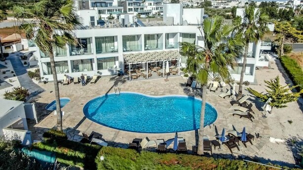 Un hôtel moderne doté d’une piscine centrale, de chaises longues et de palmiers.