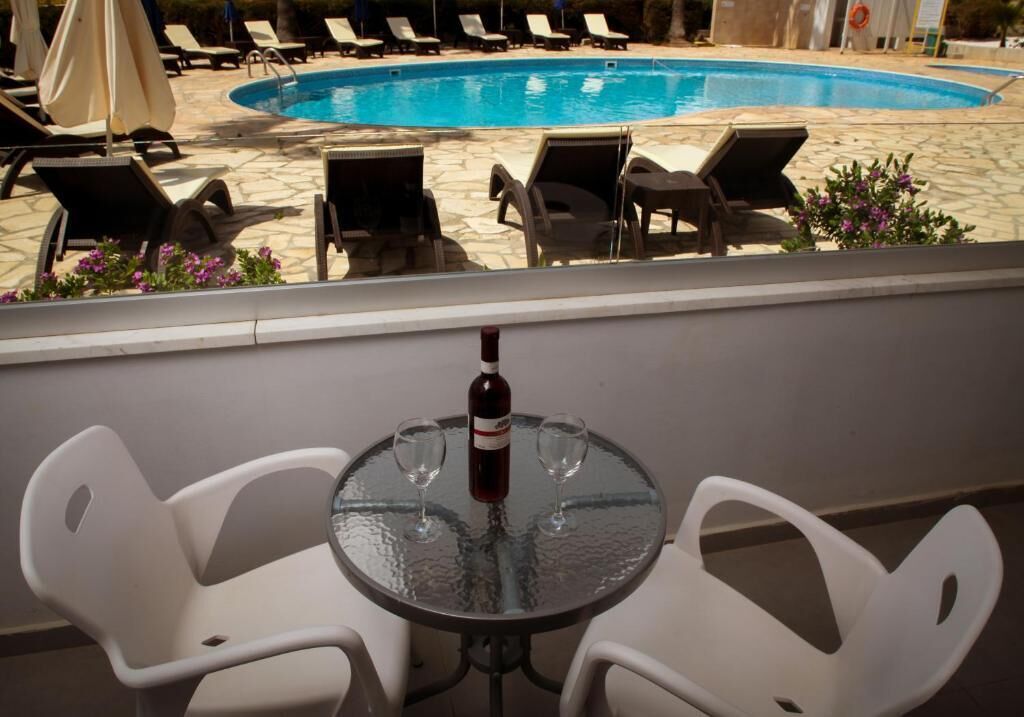 Un espace aménagé au bord de la piscine, avec des chaises longues et une table sur laquelle sont posés deux verres à vin et une bouteille.