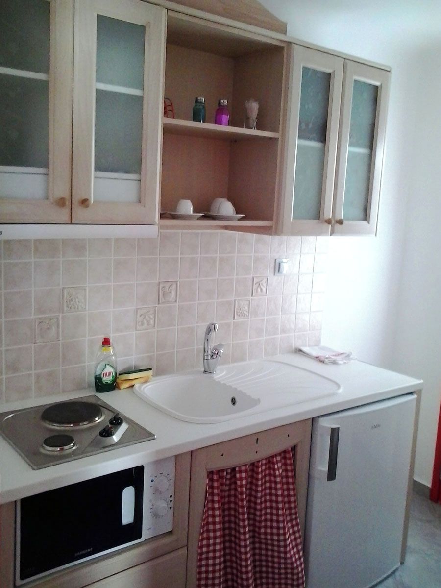 Una cocina con encimera blanca, microondas integrado y un refrigerador pequeño.