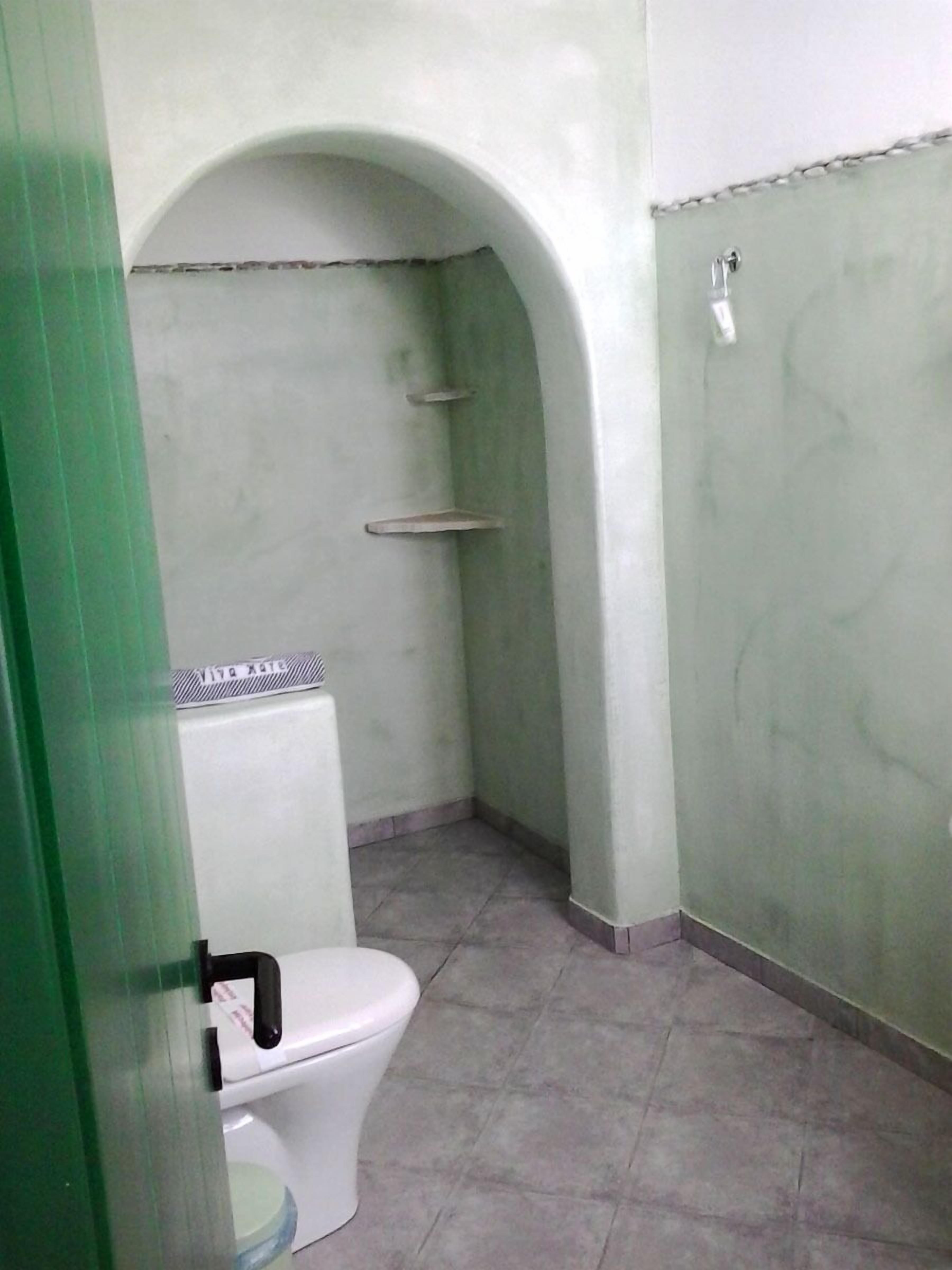 A small, enclosed bathroom with a toilet, a shower stall, and a tiled floor.