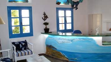 Relax in a nautical-themed room with a seascape mural, two windows offering views of lush greenery, and a comfortable chair.