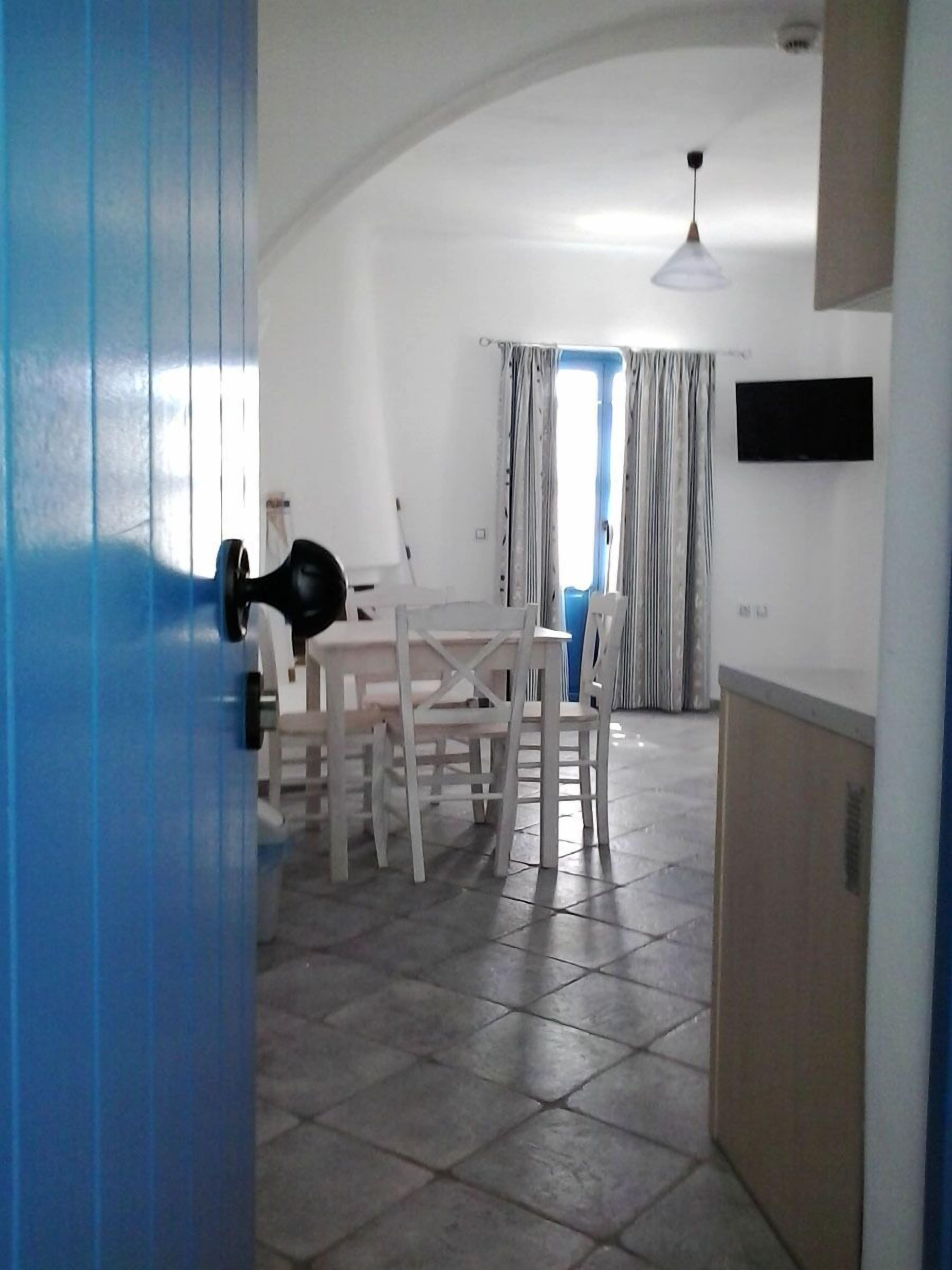 A room with a dining table, chairs, a TV mounted on the wall, and a door with a blue frame.