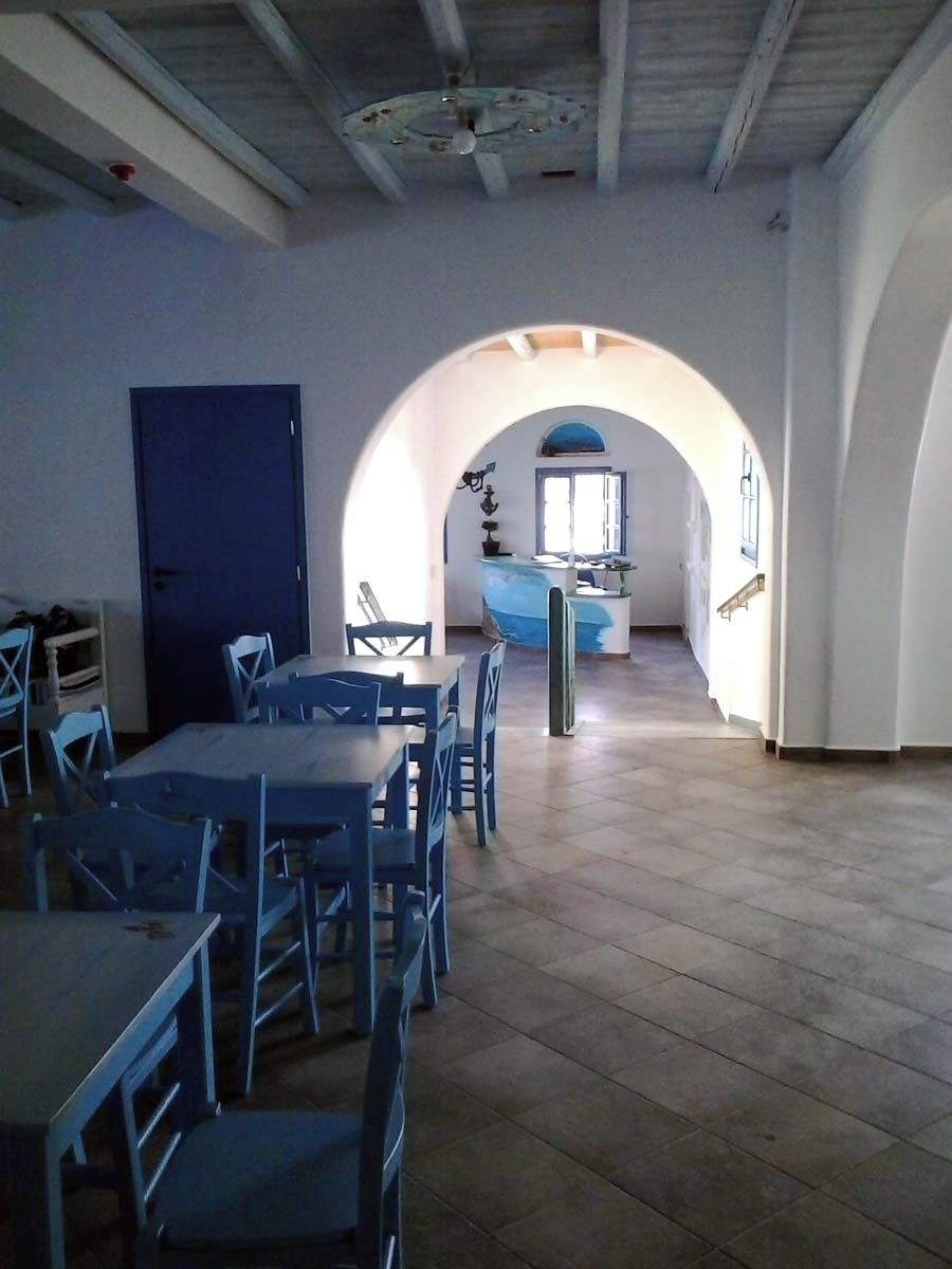 A dining area with tables and chairs, a kitchen in the background, and an arched doorway.