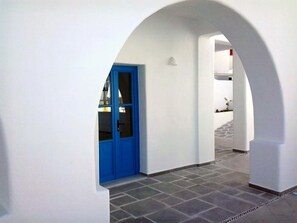 Um corredor com porta azul, paredes brancas e chão ladrilhado.