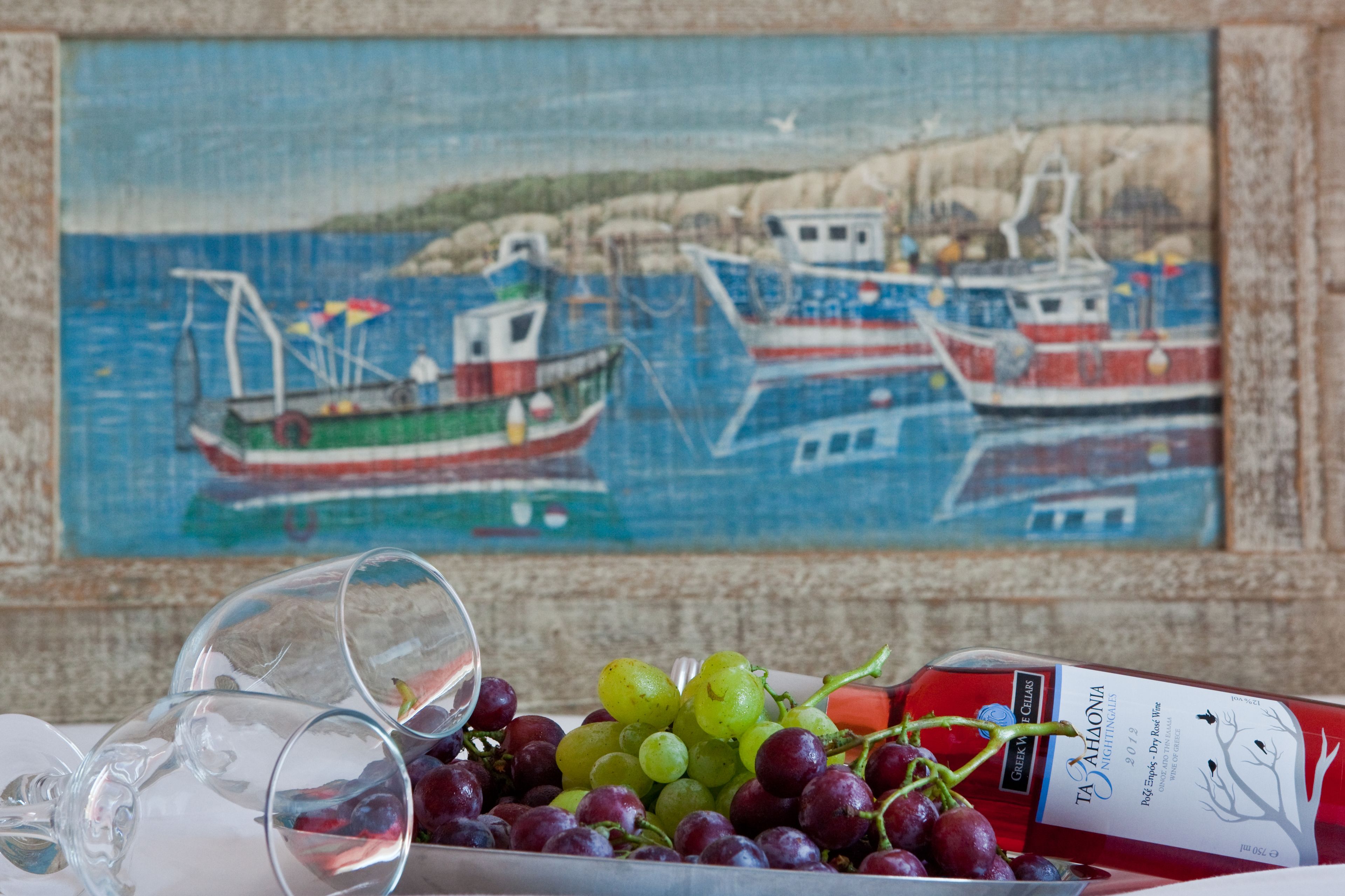 A table with a bottle of wine, a bowl of grapes, and empty wine glasses.