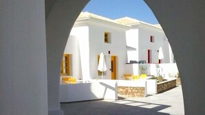 An outdoor courtyard with a white building, a stone wall, and a tiled floor. - Viva Mare Hotel (Pylos-Nestoras)