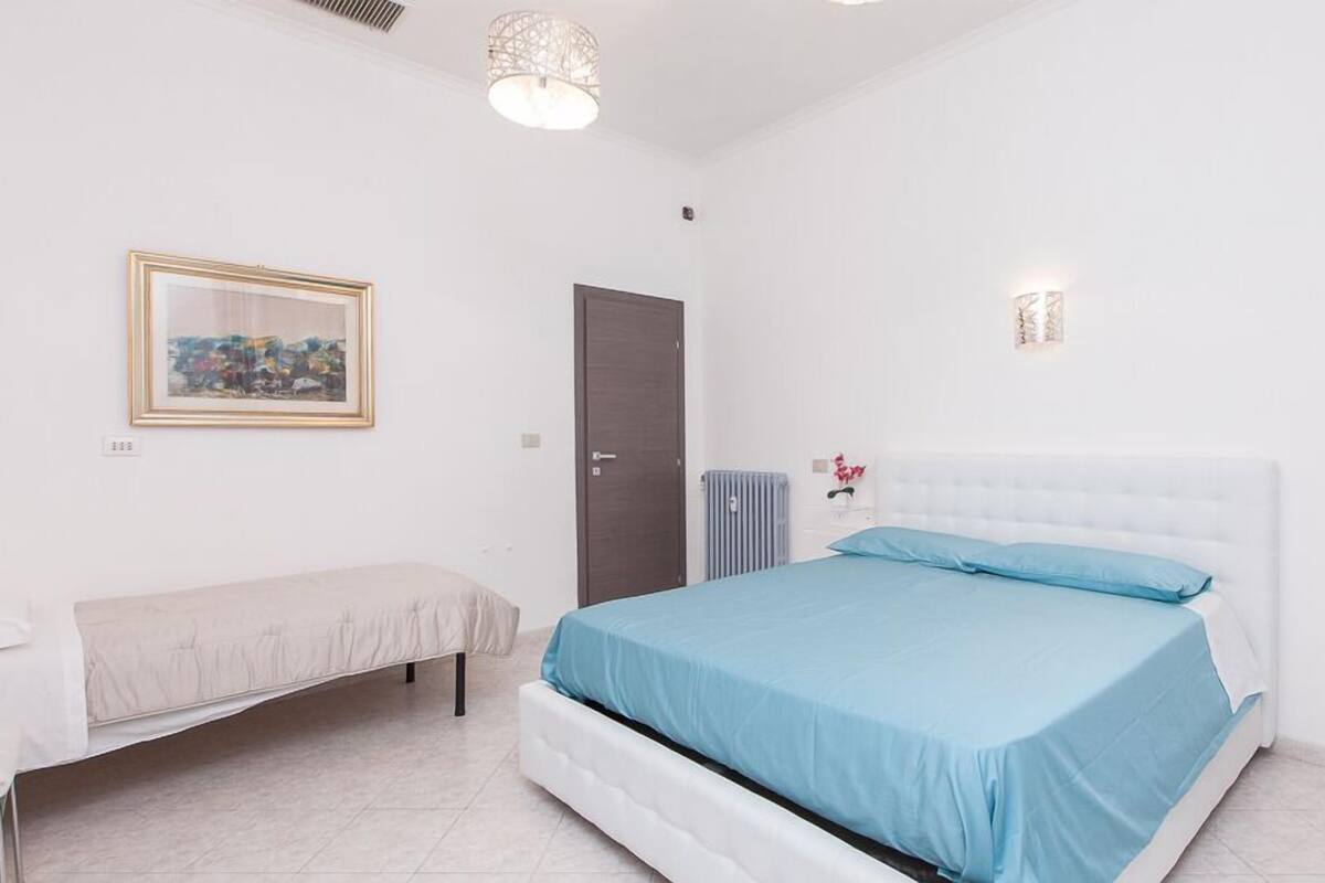 Une chambre à coucher avec un lit, une table de chevet, une chaise, un radiateur et une porte.